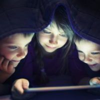 Kids secretly reading book or playing game, or watching a cartoon on digital tablet.