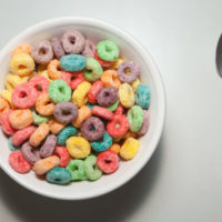 Bowl of colorful breakfast cereal with spoon on plain white background.