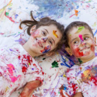 A brother and sister having a good time finger painting together.
