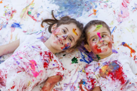 A brother and sister having a good time finger painting together.