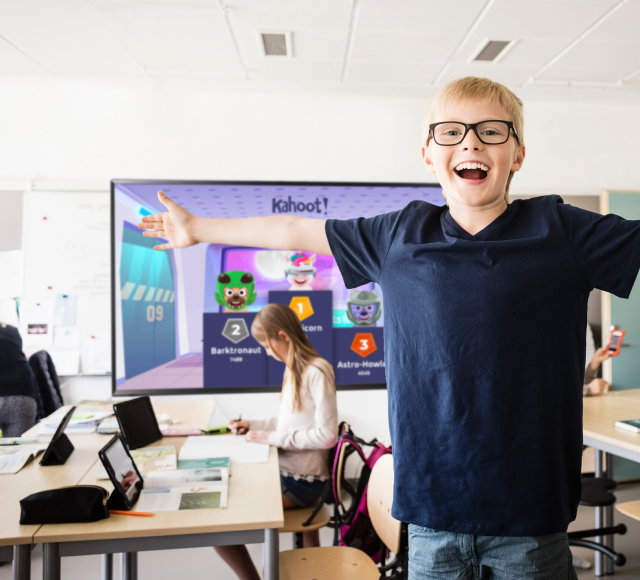 Boy in classroom with arms outstretched with kahoot podium on the screen in the background