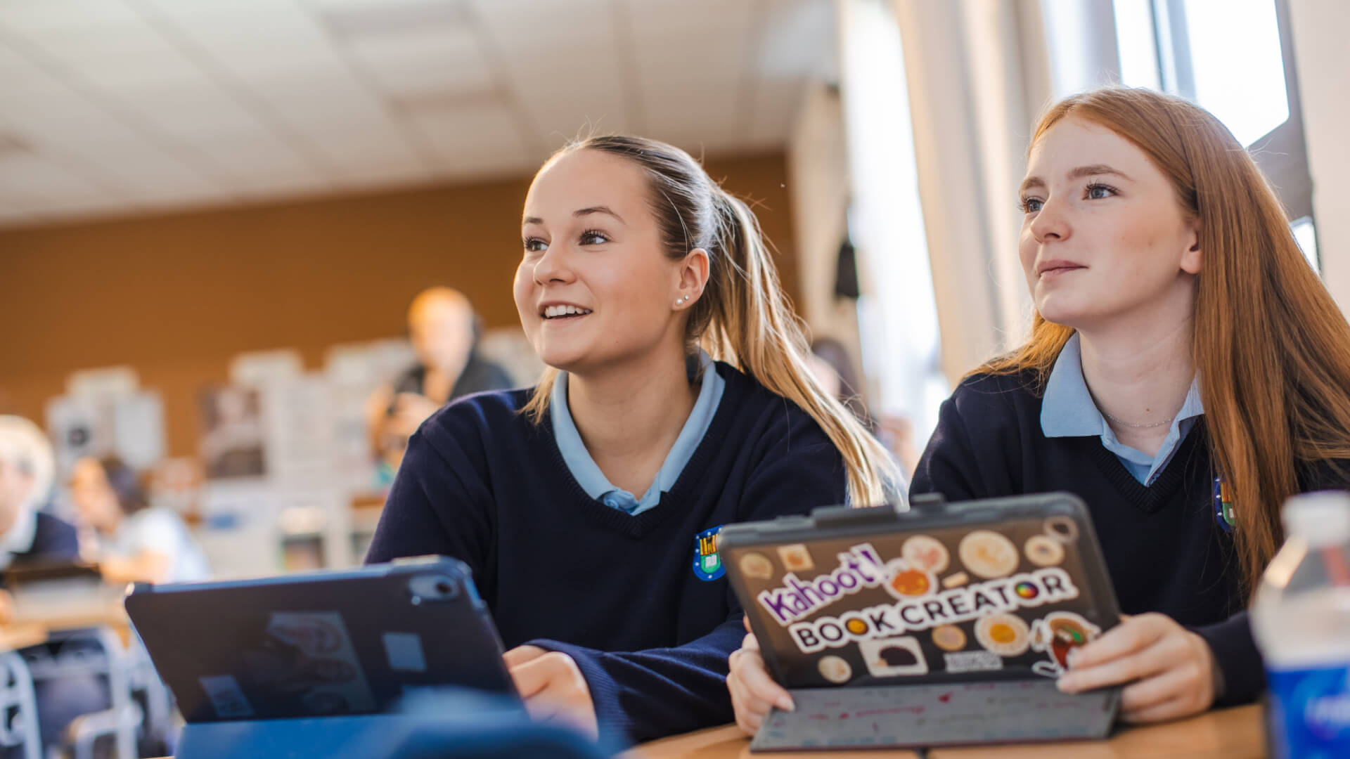 Two students in a classroom holding digital tablets