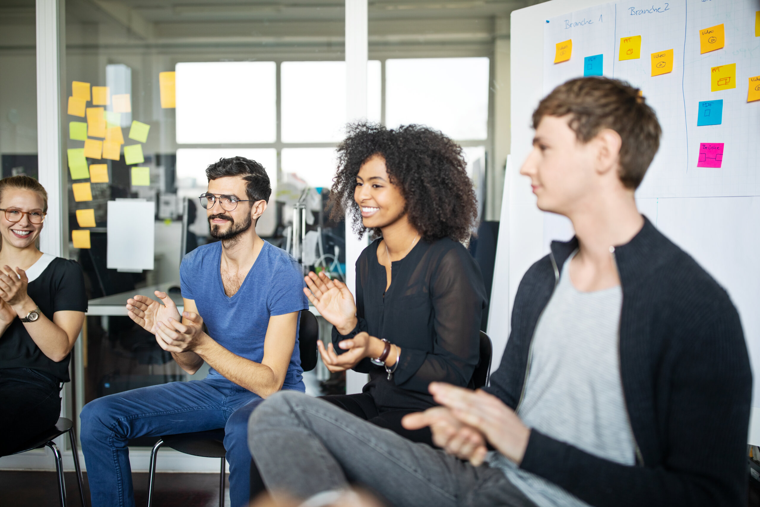Four younger professionals sitting and applauding in an office