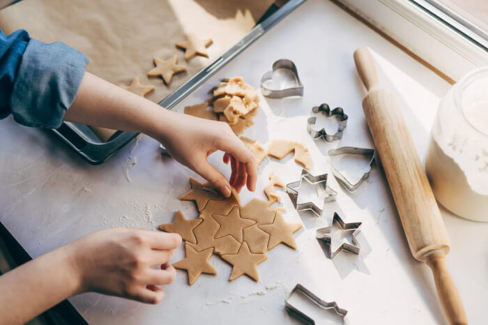 Overhead shot of hands cutting out star-shaped cookies from dough on a countertop, surrounded by metal cookie cutters and a rolling pin.