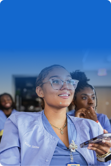 A blue-tinted photograph of healthcare students in scrubs sitting around a conference table engaged in a lively discussion, with a Kahoot! presentation visible on a screen in the background