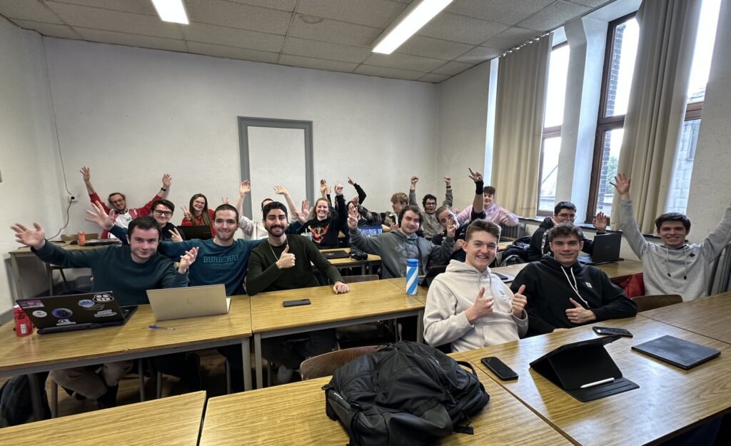 Group of students in lines of desks, cheering for camera 