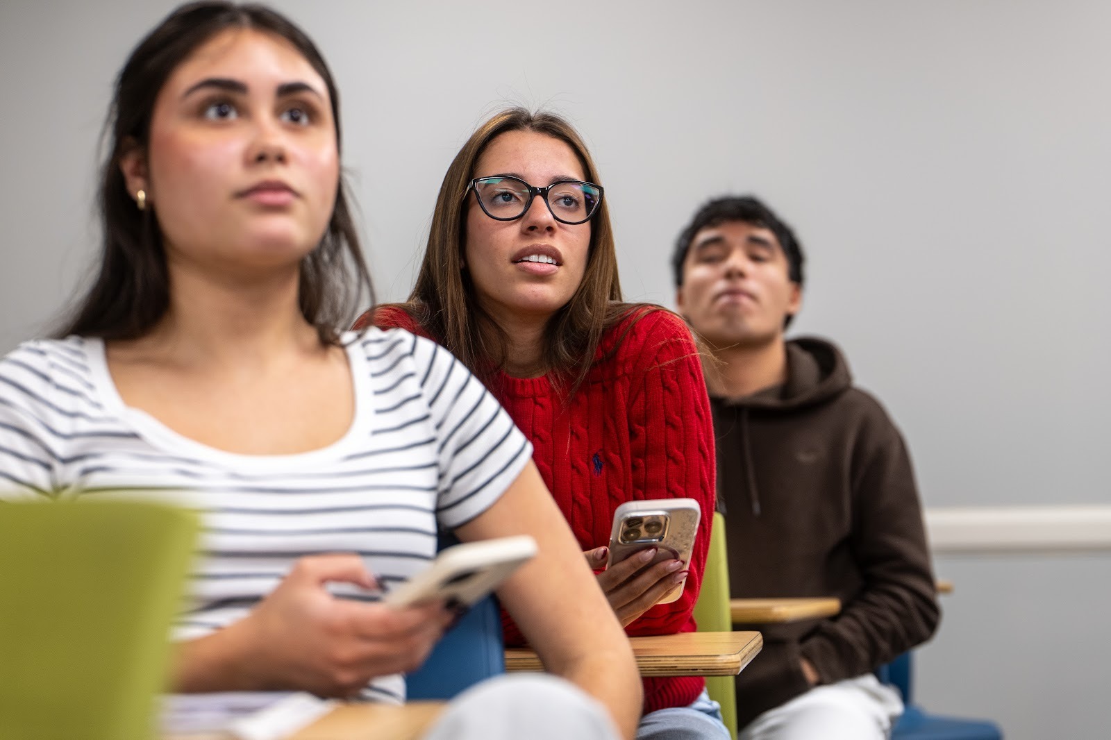 A close-up shot of three students seated in a classroom, captured from a slightly low angle.