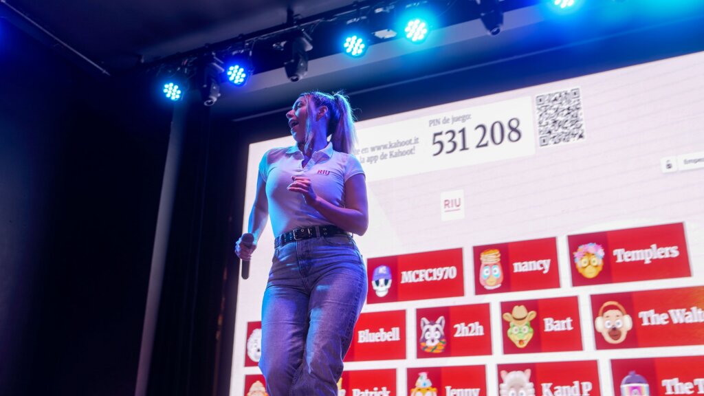 A female RIU entertainer is on stage engaging an audience using Kahoot! .