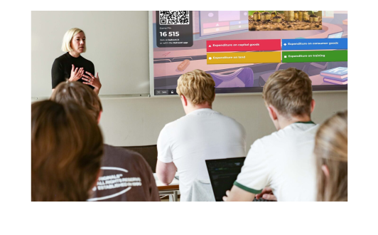 A university lecturer presents a Kahoot! quiz to students in a lecture hall, with the game displayed on a large screen behind her.