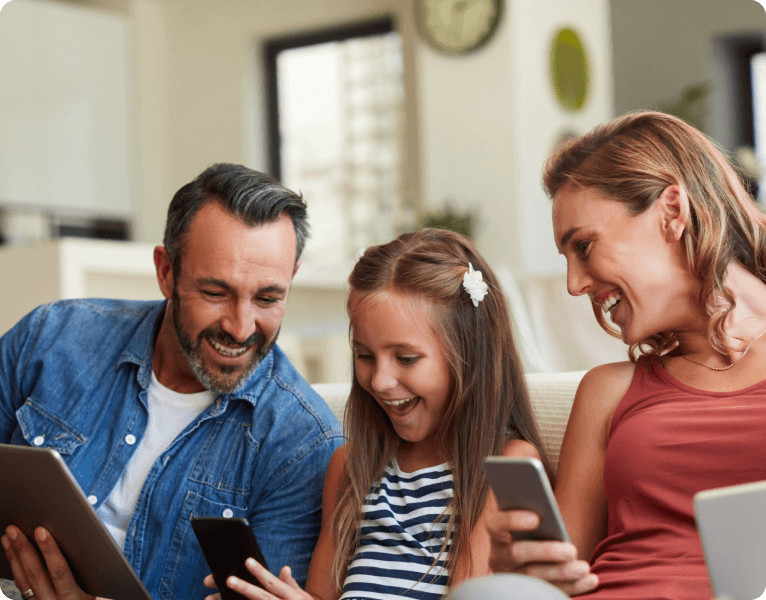 Family of three laughing together while using phones and a tablet at home