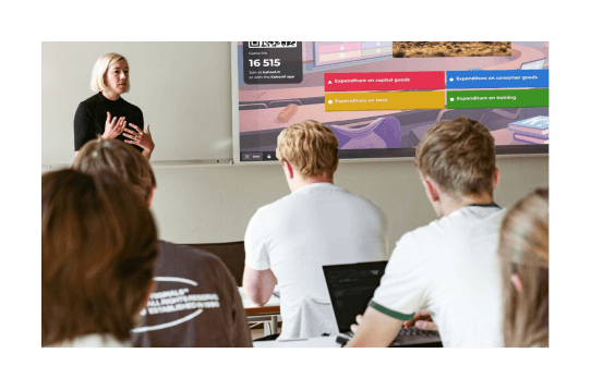 A group of university students smile and work together on laptops during a Kahoot! session in a bright classroom.