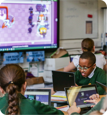 Young girl raising her hand enthusiastically in a classroom with a tablet on her desk