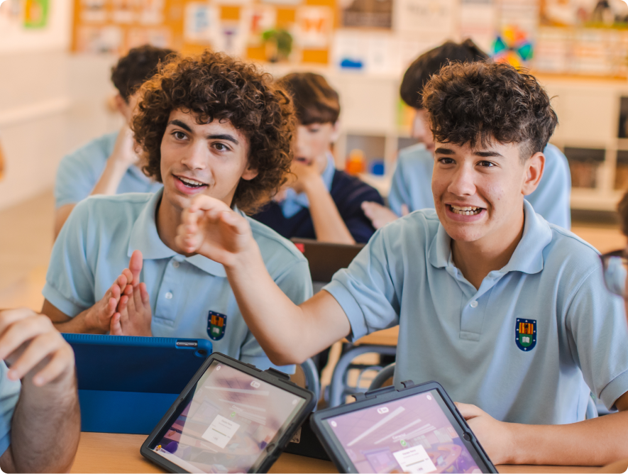 Two male students in school uniforms engaged with tablets, one pointing enthusiastically