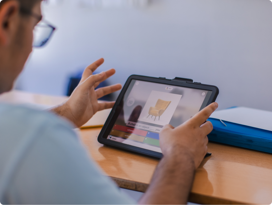 Student gesturing with hands while looking at a Kahoot question showing a chair image on a tablet
