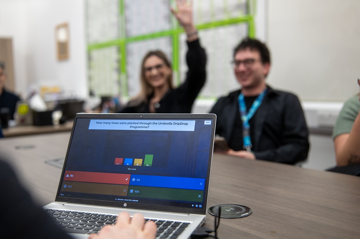 Employees seated around a meeting table with a laptop displaying a kahoot session