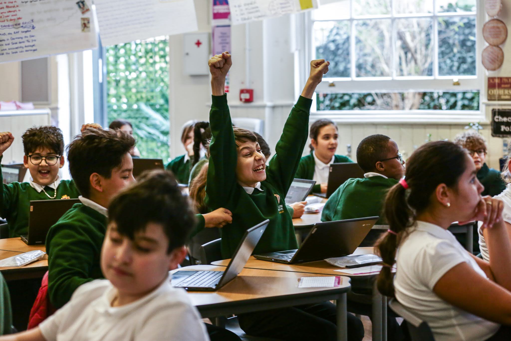 A student raising fists in celebration next to classmates in a classroom