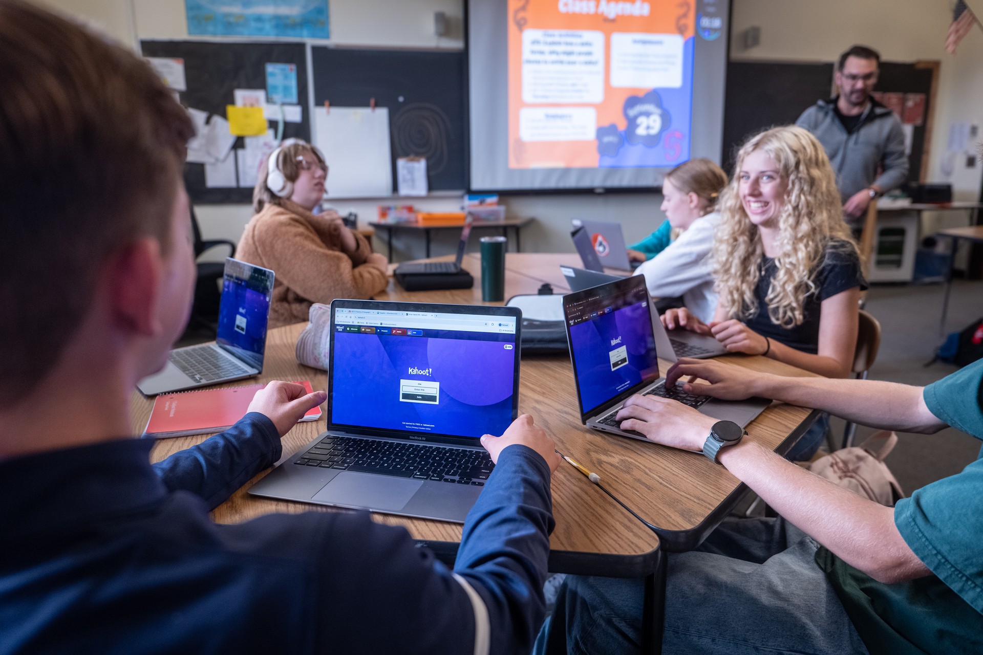Students in a classroom interacting with laptops. The teacher is at the front of the class and they are all learning through playing a Kahoot!