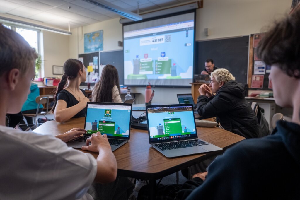 9th grade students have their computers at their desks and they are learning with Kahoot! with the teacher in front of the classroom. 
